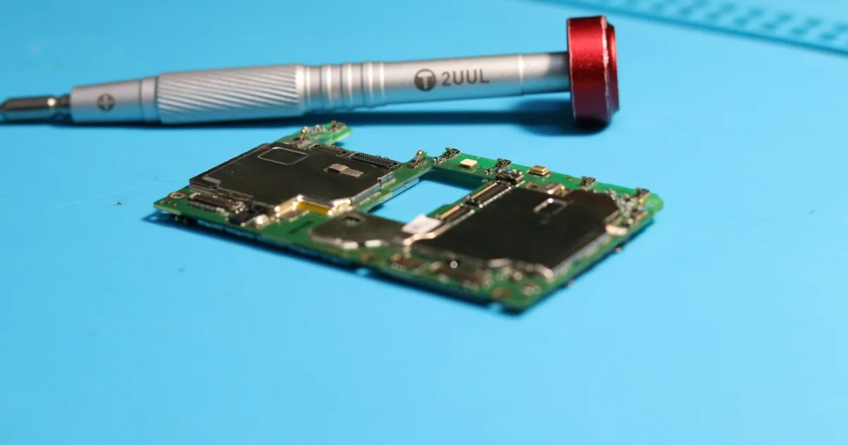 Close-up of a small circuit board and a precision screwdriver on a blue mat