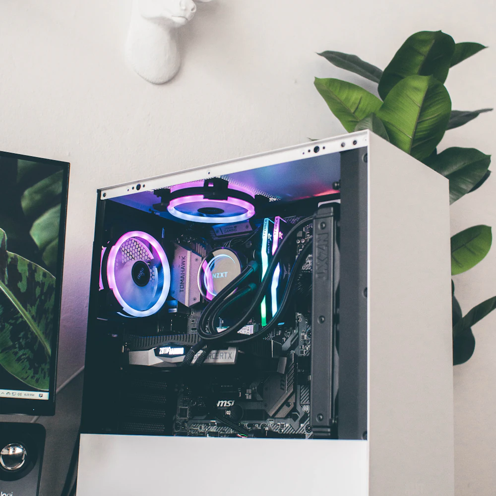 White mid-tower gaming PC with RGB fans beside a monitor and plant